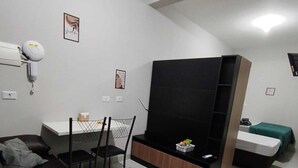 Uma sala de estar moderna com um sofá, uma mesa de jantar com cadeiras, um rack para TV e uma pequena área de cozinha.