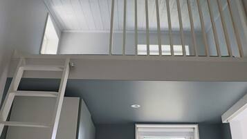 Una habitación con ventana, una escalera blanca y un respiradero en el techo.
