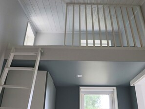 Ein Zimmer mit Fenster, einer weißen Treppe und einem Lüftungsgitter an der Decke.