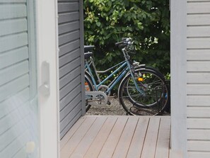 Una bicicleta estacionada en una terraza de madera, con una puerta que da a un espacio cubierto.