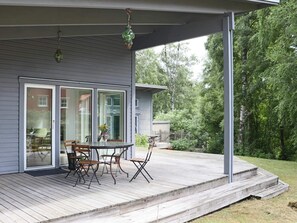 Una terraza techada al aire libre con una mesa y sillas, un farol colgante y vistas a un área boscosa.