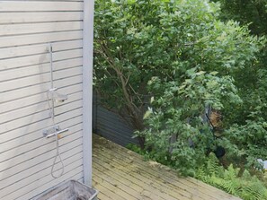 Eine Holzterrasse mit einem Metall-Wasserhahn an der Gebäudeseite.