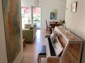 Ein Zimmer mit Klavier, einer Couch, einem Esstisch mit Stühlen und Blick durch eine Glastür.