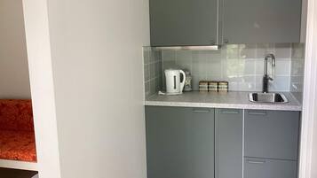 Una cocina compacta con gabinetes grises, una encimera blanca, una tetera, una caja pequeña y un lavabo.