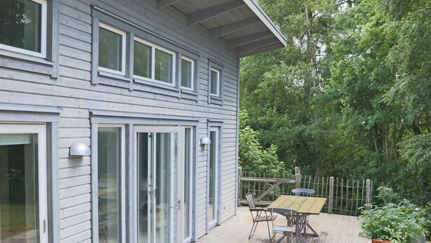 Et hus med terrasse, skydedøre og et træhegn.