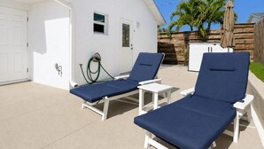 A white building with a garage, two lounge chairs, a small table, and a wooden fence with palm trees. - 🏖️3BD/2BA Walk to Beach & Downtown / Pool / 349NO (Cocoa Beach)