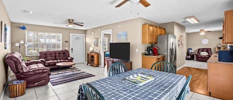 A compact living space with a dining area, a sofa, a television, and a kitchen area with cabinets and a refrigerator.