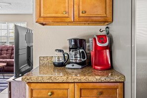 A kitchen with granite countertop, a coffee maker, a glass carafe, and a refrigerator.