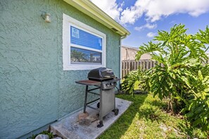 A house with a blue exterior, a barbecue grill, and a window with a sign.