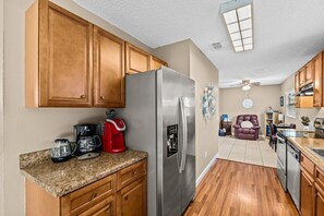 A kitchen with wooden cabinets, a stainless steel refrigerator, a coffee maker, and a dining area with a leather couch.