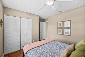 Un dormitorio con cama, ventilador de techo, armario y cuadros en la pared.