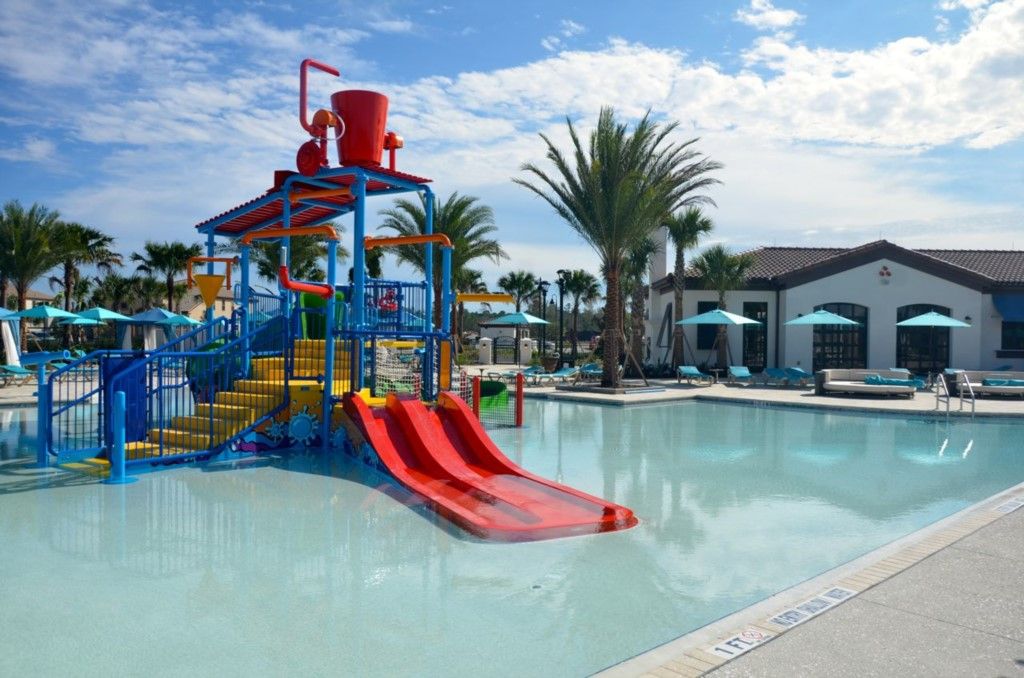 A water park with a red slide, blue and yellow play structures, and a pool area with lounge chairs and umbrellas.