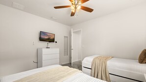 Un dormitorio con dos camas, un ventilador de techo, un televisor, un aparador y una puerta.