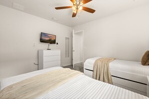 Ein Schlafzimmer mit zwei Betten, einem Deckenventilator, einem Fernseher, einem Schminktisch und einer Tür.
