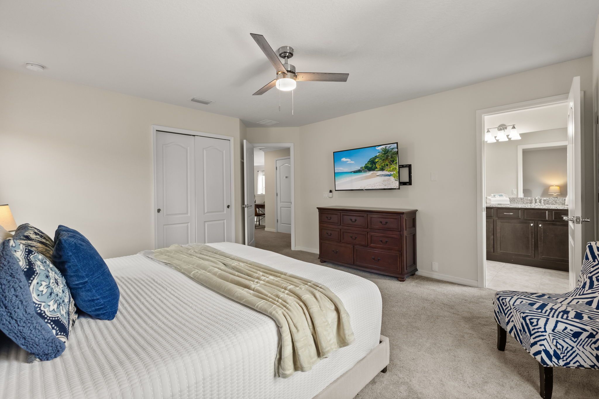 A bedroom with a bed, a ceiling fan, a TV, a dresser, and a chair.