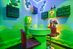 Quarto com uma mesa verde, duas cadeiras e decoração temática do Mario.