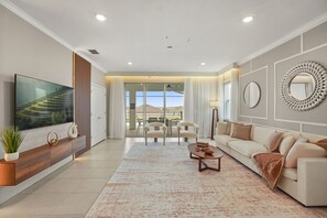 Una sala de estar moderna con un televisor de pantalla plana, un sofá, una mesa de centro y vistas al exterior.