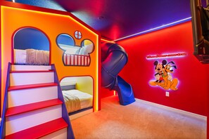 Ein Spielbereich für Kinder mit einer Rutsche, einem Bett und einer Wand mit Aufklebern von Mickey Mouse und Minnie Mouse.