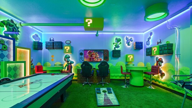 Ein Raum mit Billardtisch, zwei Spielsesseln und einem großen Bildschirm, der ein Videospiel zeigt.