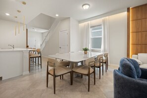 Eine moderne Küche mit einer zentralen Kochinsel, einem Essbereich mit rundem Tisch und Stühlen sowie einer Treppe, die eine weitere Ebene hinaufführt.