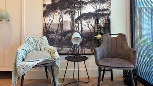 A room with a large painting of trees, a lamp on a small table, and two chairs.