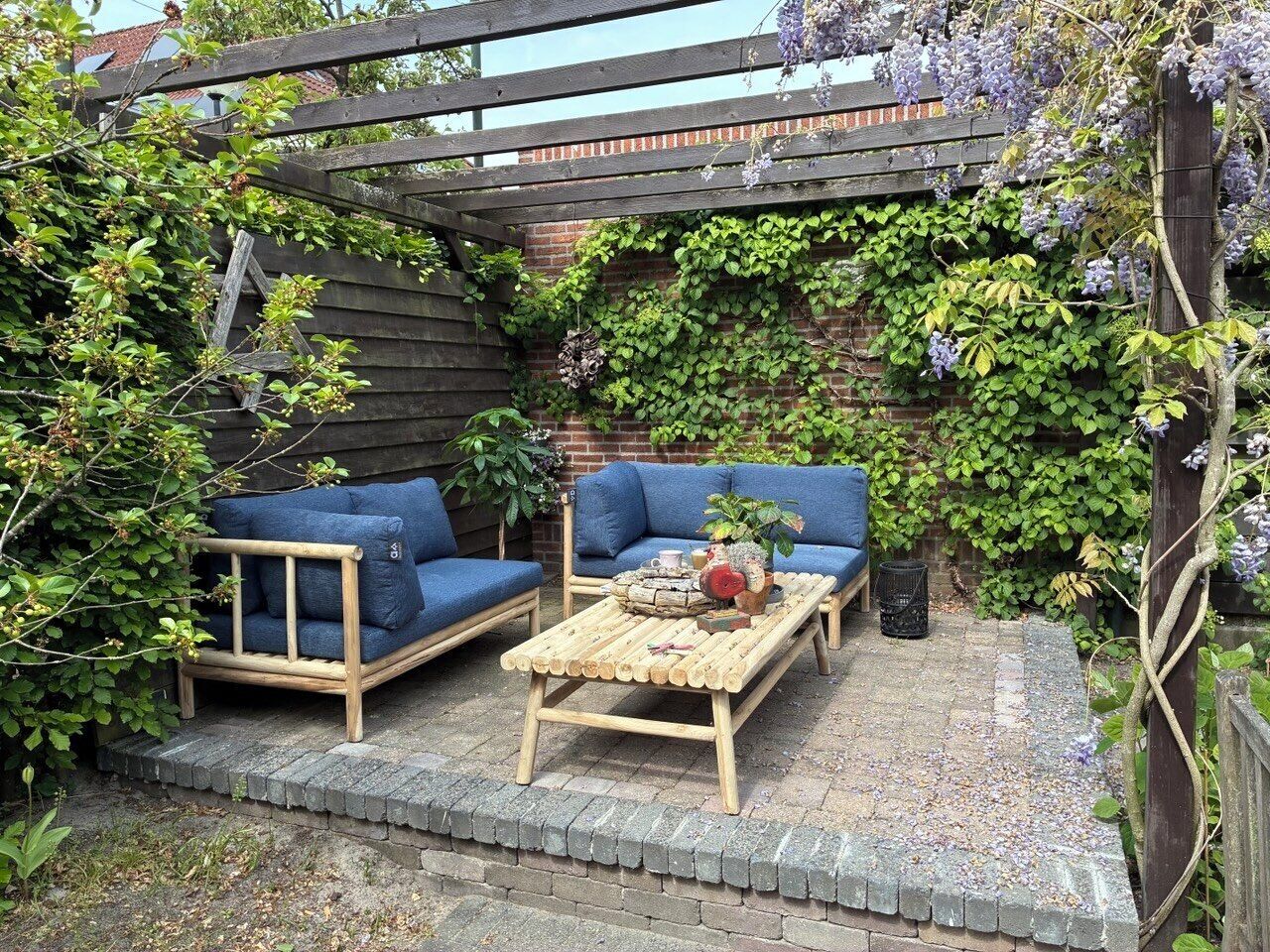 A wooden bench, two blue sofas, and a table with a vase and books in a garden setting.