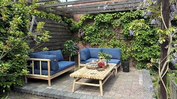 A wooden bench, two blue sofas, and a table with a vase and books in a garden setting.