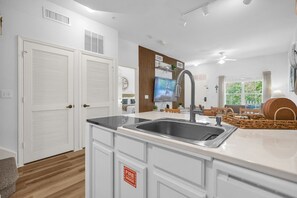 A modern kitchen with white cabinetry, a stainless steel sink, and a flat-screen TV mounted above the counter. - Family Comfort House / Sleeps 6  - 31-106 (Kissimmee)