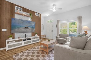 Ein Wohnzimmer mit Flachbildfernseher, einer Holz-Unterhaltungsecke, einer Couch, einem Couchtisch und einem Fenster mit Vorhängen.
