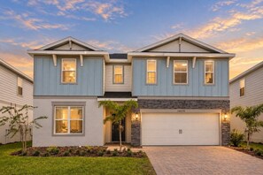 A two-story house with a garage, a driveway, and a well-maintained lawn. - Immersive Themed Bedrooms 10 BD/ 8 BA/ Windsor Cay - 16030CC (Clermont)