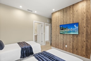 Ein Hotelzimmer mit zwei Betten, einer Wand mit Holzvertäfelung und einem Fernseher, der eine tropische Strandlandschaft zeigt.
