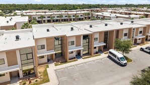 Um complexo moderno de apartamentos com várias unidades, uma área de estacionamento e um veículo.