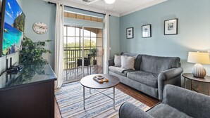 Ein Wohnzimmer mit grauem Sofa, einem Couchtisch, einem Fernseher und einem Balkon mit Blick.