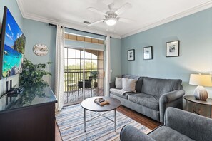Ein Wohnzimmer mit grauem Sofa, einem Couchtisch, einem Fernseher und einem Balkon mit Blick.