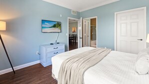 Ein Schlafzimmer mit Bett, einem Schminktisch, einem an der Wand befestigten Fernseher und einer Tür zu einem Badezimmer.