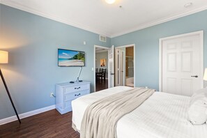 Ein Schlafzimmer mit Bett, einem Schminktisch, einem an der Wand befestigten Fernseher und einer Tür zu einem Badezimmer.