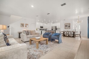 Ein modernes Wohnzimmer mit Sofa, Sesseln, einem Couchtisch und einem Essbereich mit Tisch und Stühlen.