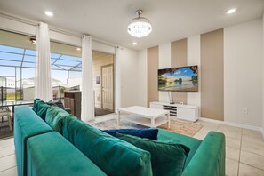 Een moderne woonkamer met een groene bank, een witte salontafel en een televisie aan de muur.