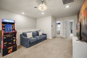 Ein Wohnzimmer mit einem blauen Sofa, einer Spielkonsole, einem Chandelier und einem Fernseher.
