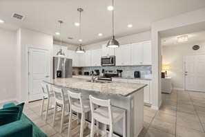 A modern kitchen with white cabinetry, stainless steel appliances, and a granite island with bar stools. - Modern +  Private Pool 5 BD/ 4.5 BA Windsor Island Resort  - 3745 PL (Davenport)