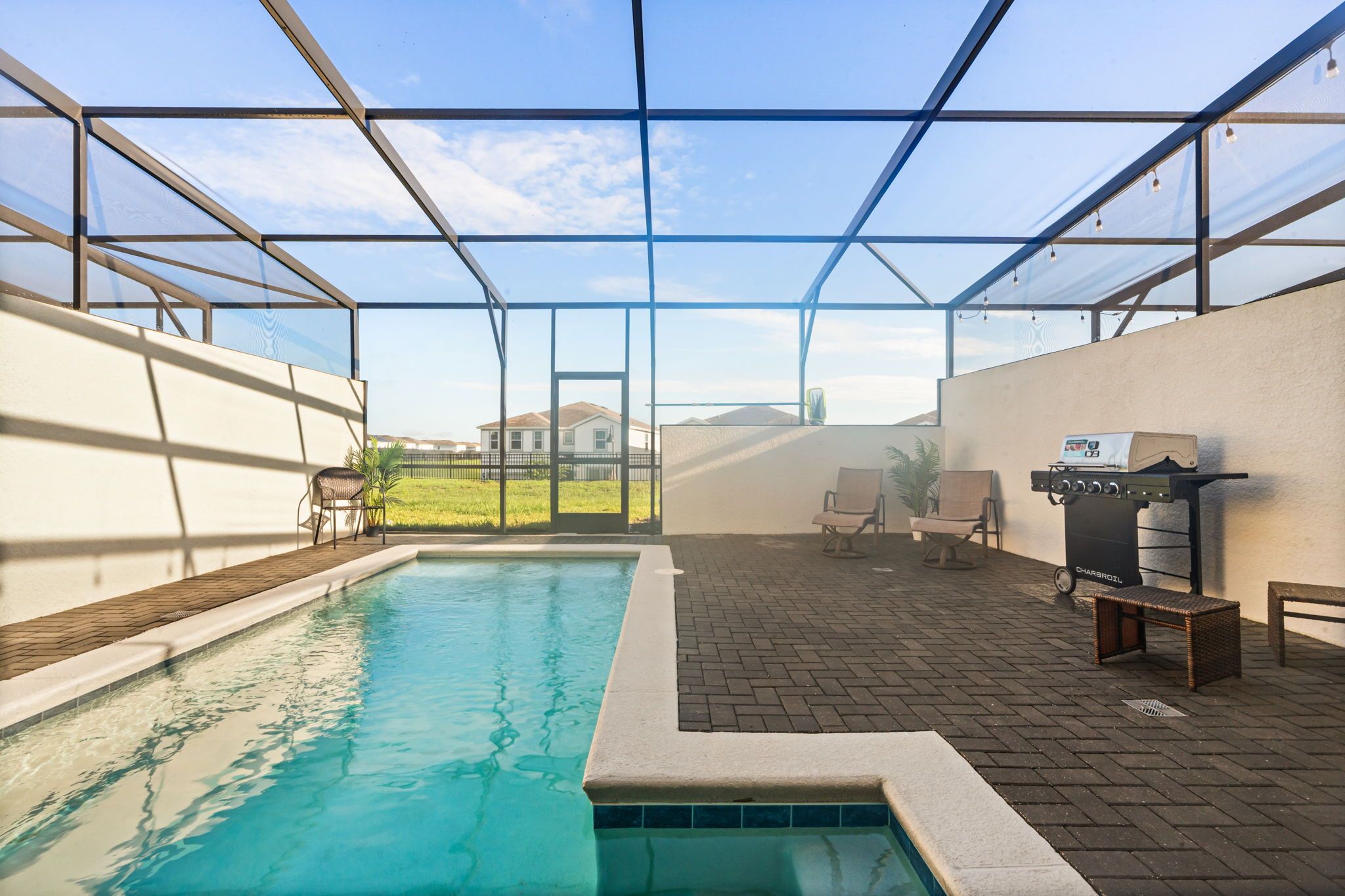 Un espace piscine intérieure doté d’une paroi vitrée, d’un barbecue et de coins salon.