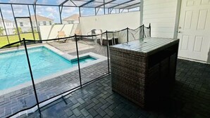 Ein überdachter Außenbereich mit Pool, einem Korbstuhl-Tisch und einer Tür.
