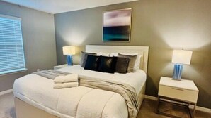 Ein Schlafzimmer mit einem großen Bett, zwei Nachttischen, einem Deckenventilator und einem an der Wand befestigten Kunstwerk.