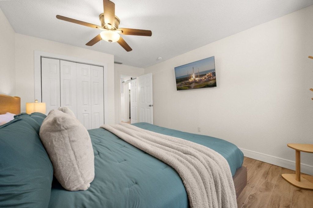 Un dormitorio con cama, ventilador de techo, puerta y un cuadro en la pared.