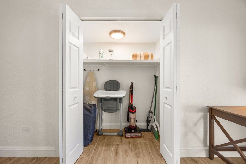 Un couloir étroit avec un luminaire au plafond, une petite étagère contenant des produits de nettoyage et un aspirateur.