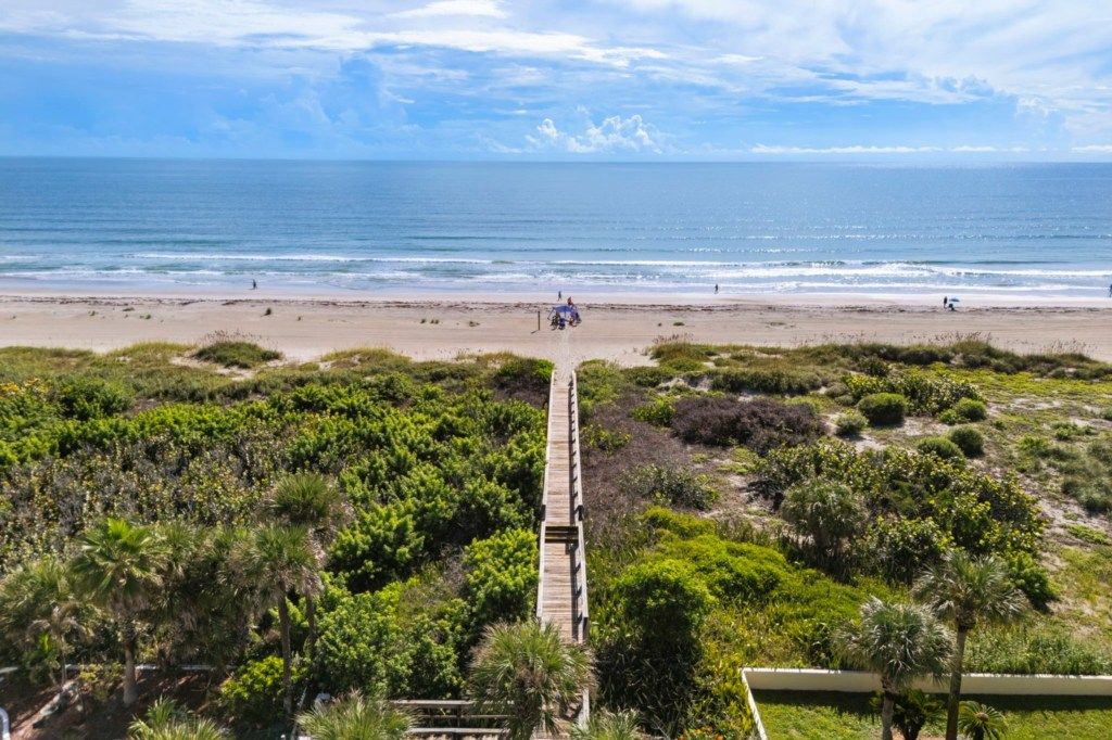 A beach with a wooden boardwalk leading to the shore, surrounded by dense greenery.