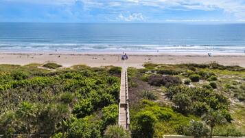 A beach with a wooden boardwalk leading to the shore, surrounded by dense greenery.