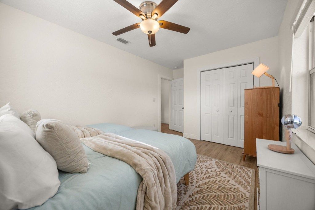 Une chambre à coucher comprenant un lit, un ventilateur de plafond, une armoire en bois et une table de chevet avec une lampe.
