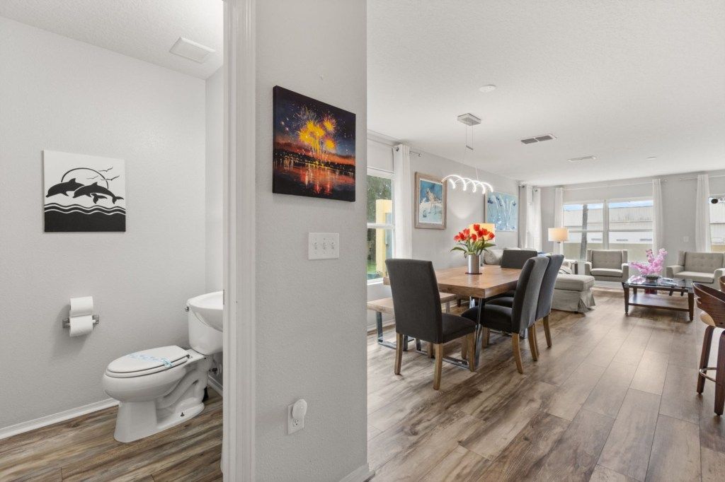A modern living room with a dining area, a white toilet, and artwork on the walls.