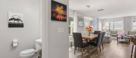A modern living room with a dining area, a white toilet, and artwork on the walls.